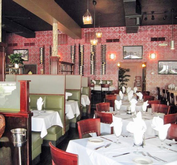 The dining room with patterned red walls, wine racks, green booths and white tablecloths