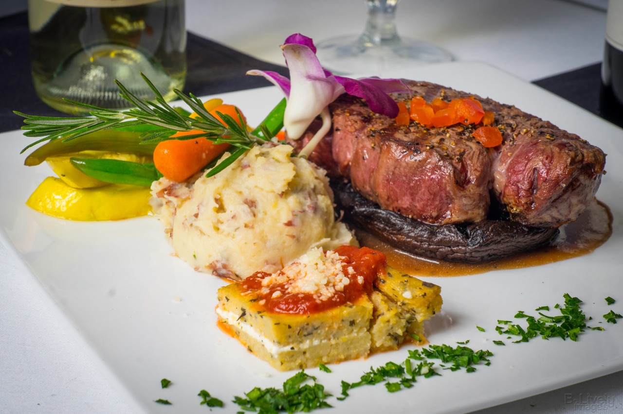 A seared filet mignon on a portobello cap with mashed potatoes, vegetables and rosemary
