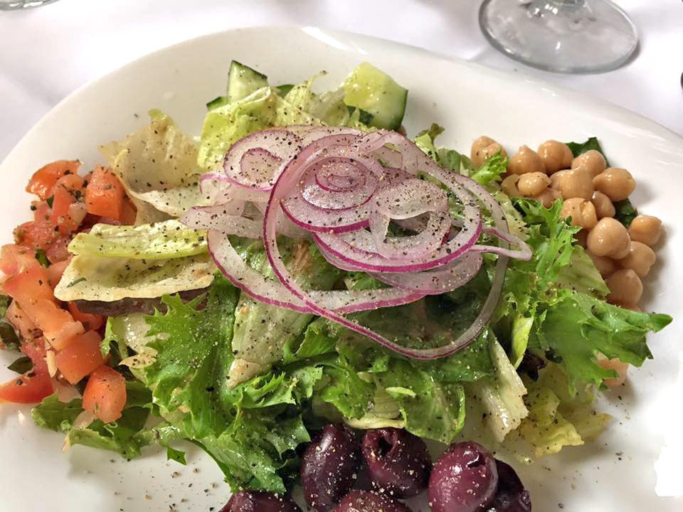 A green salad with sliced red onion, tomato, chickpeas and kalamata olives