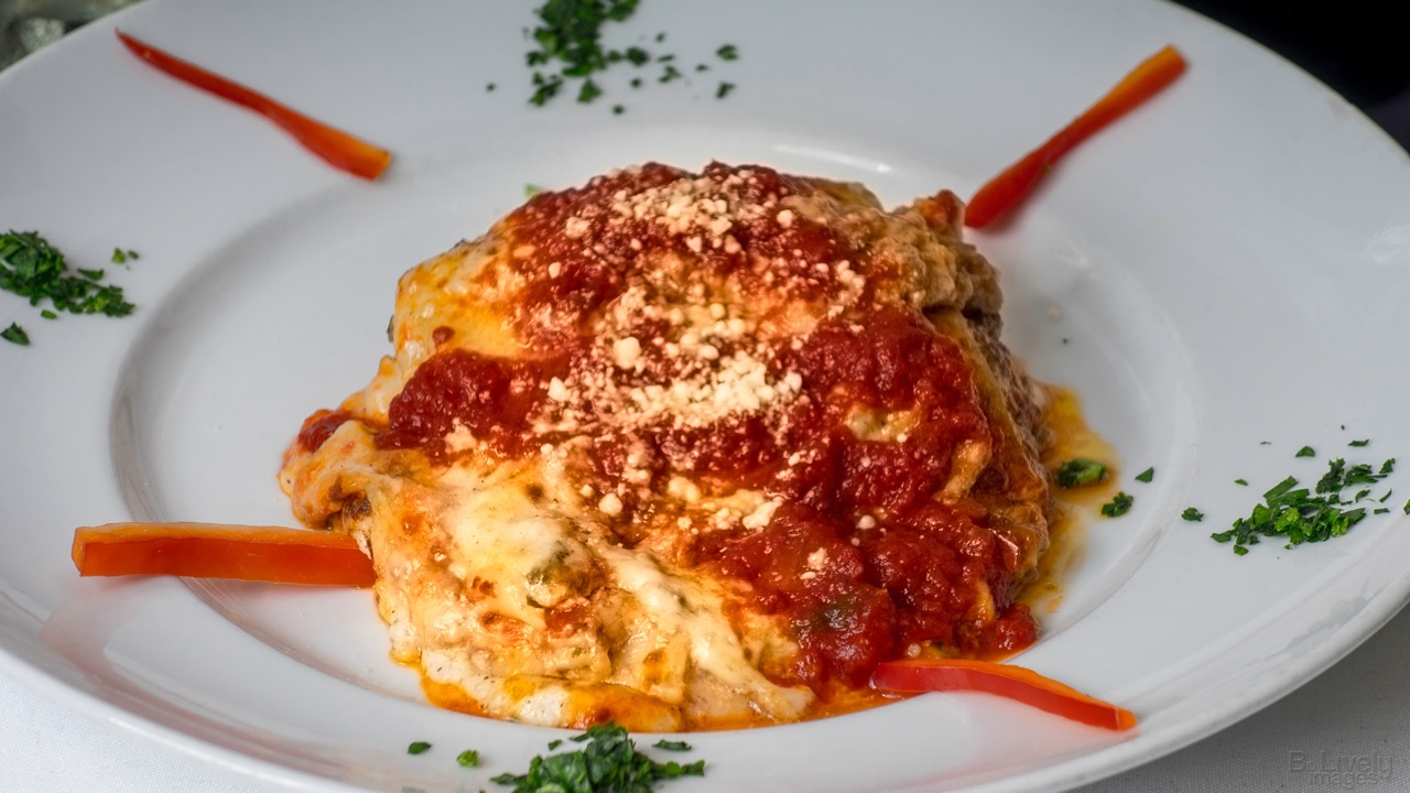 A square of lasagna under red sauce and grated parmesan on a white plate