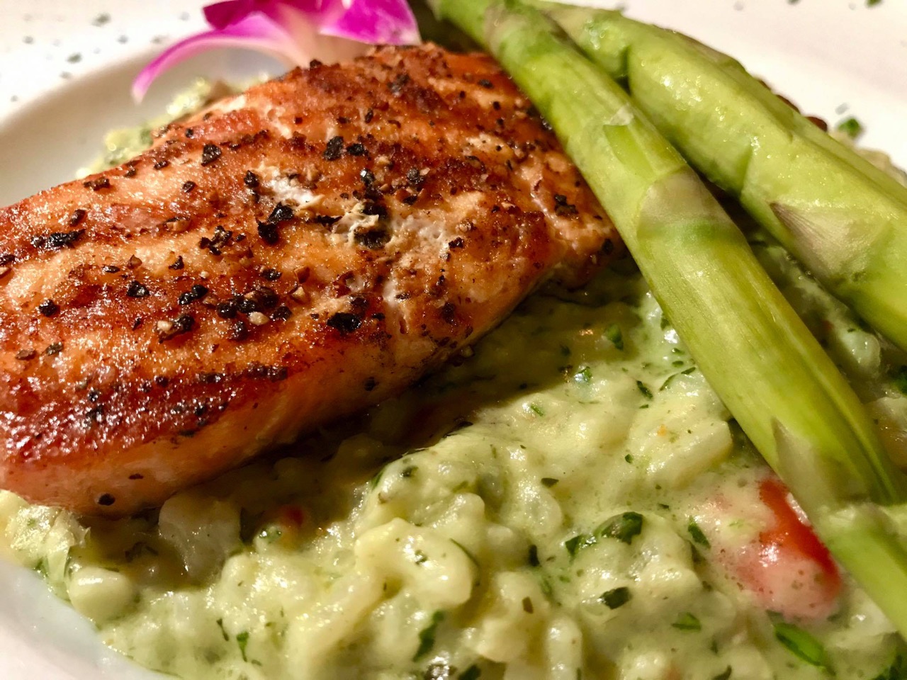 Grilled salmon and asparagus spears resting on creamy green pesto risotto