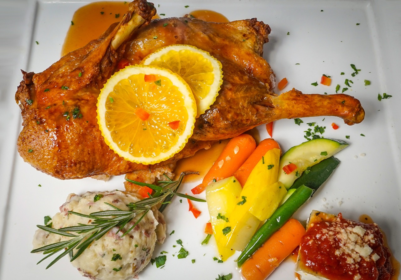 Crispy roasted half duck topped with orange slices, with mashed potatoes and vegetables