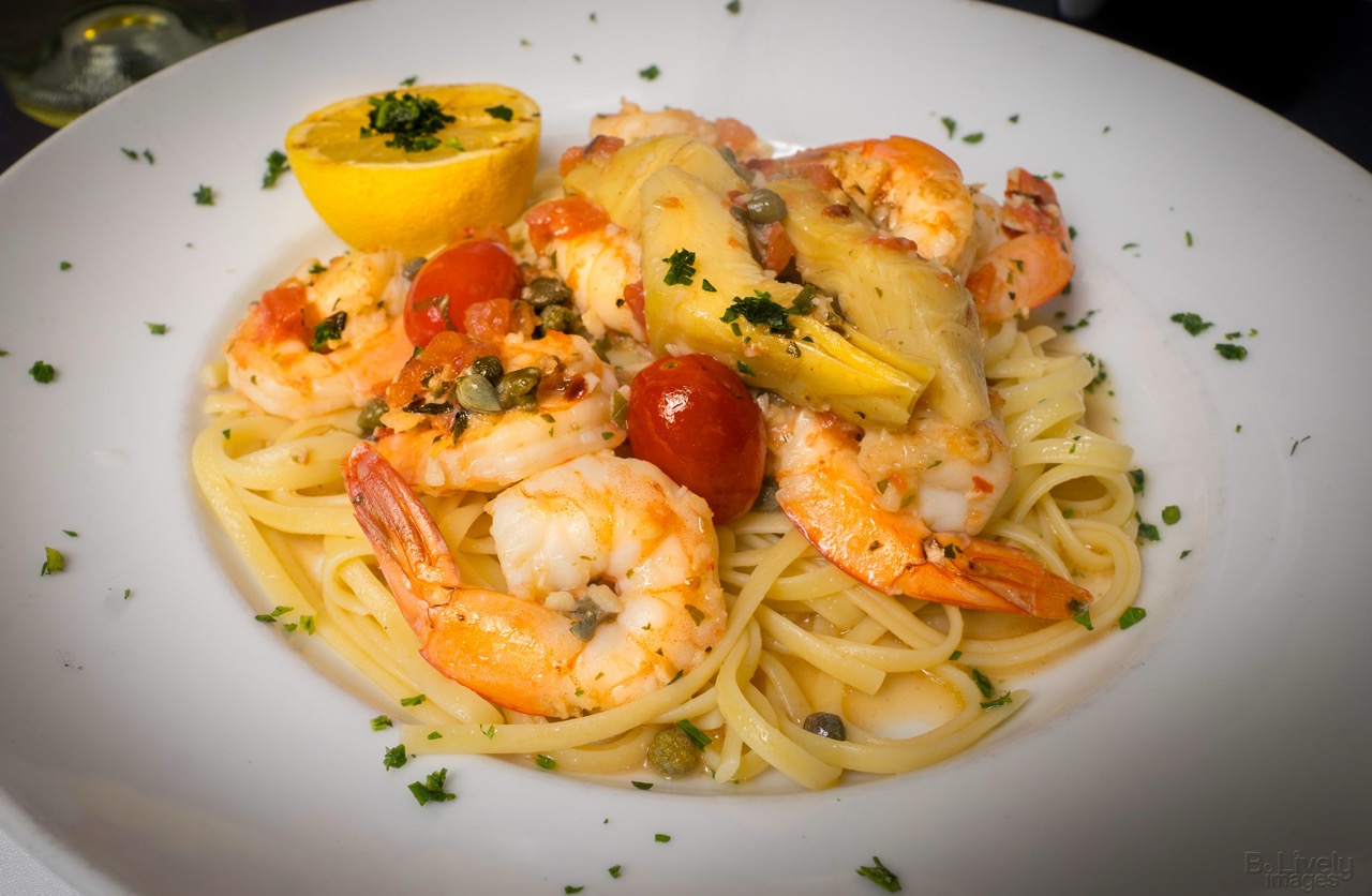 Shrimp scampi over linguine with artichokes, capers, roasted tomatoes and a lemon half